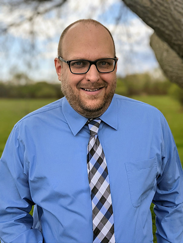 Photo of Jamie Schrauth outdoors in a shirt and tie.